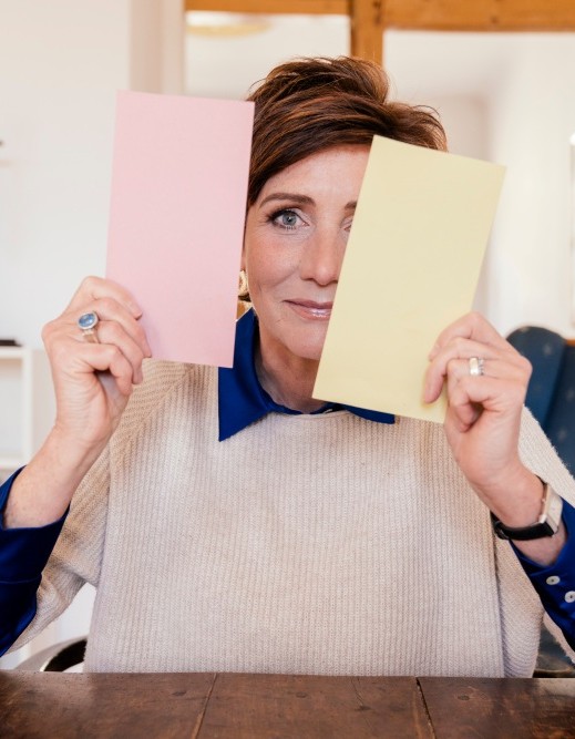 Angela Elis lächelt und hält zwei farbige Karten vors Gesicht